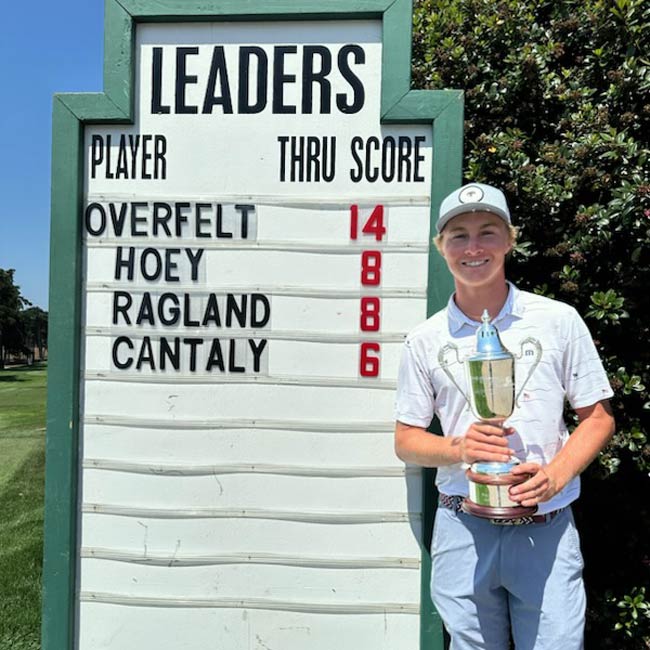 Calder Overfelt 2024 Bayonet Black Horse Amateur Champion Holding Winner Trophy in Front of Scorebaord